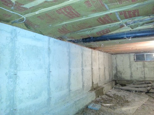 This is what our crawlspace looks like. The stuff just overhead is fiberglass insulation under the bedroom floor. On the other side of the black drain pipe is the uninsulated floor of the enclosed porch. On the left is the poured concrete wall of the foundation. The dirt floor once had plastic over it, but I found it bunched up in the corner. Some previous owner had chucked a bunch of stuff down there like bikes, old fence posts, chicken wire...